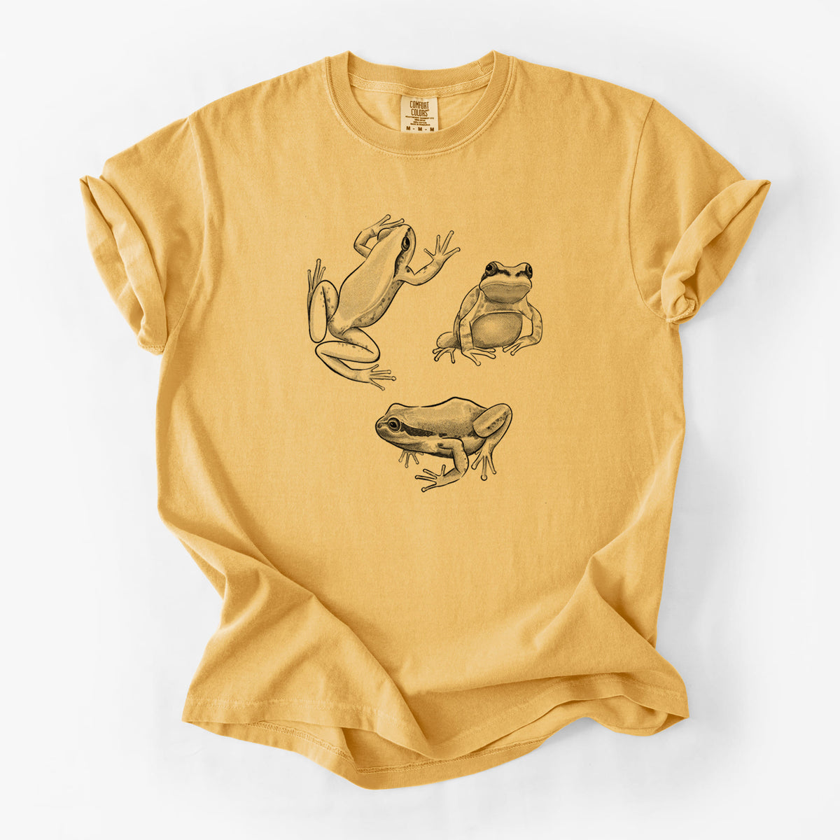 Golden wheat yellow Comfort Colors t-shirt laid flat, printed with a black ink illustration of three Pacific tree frogs in different poses.