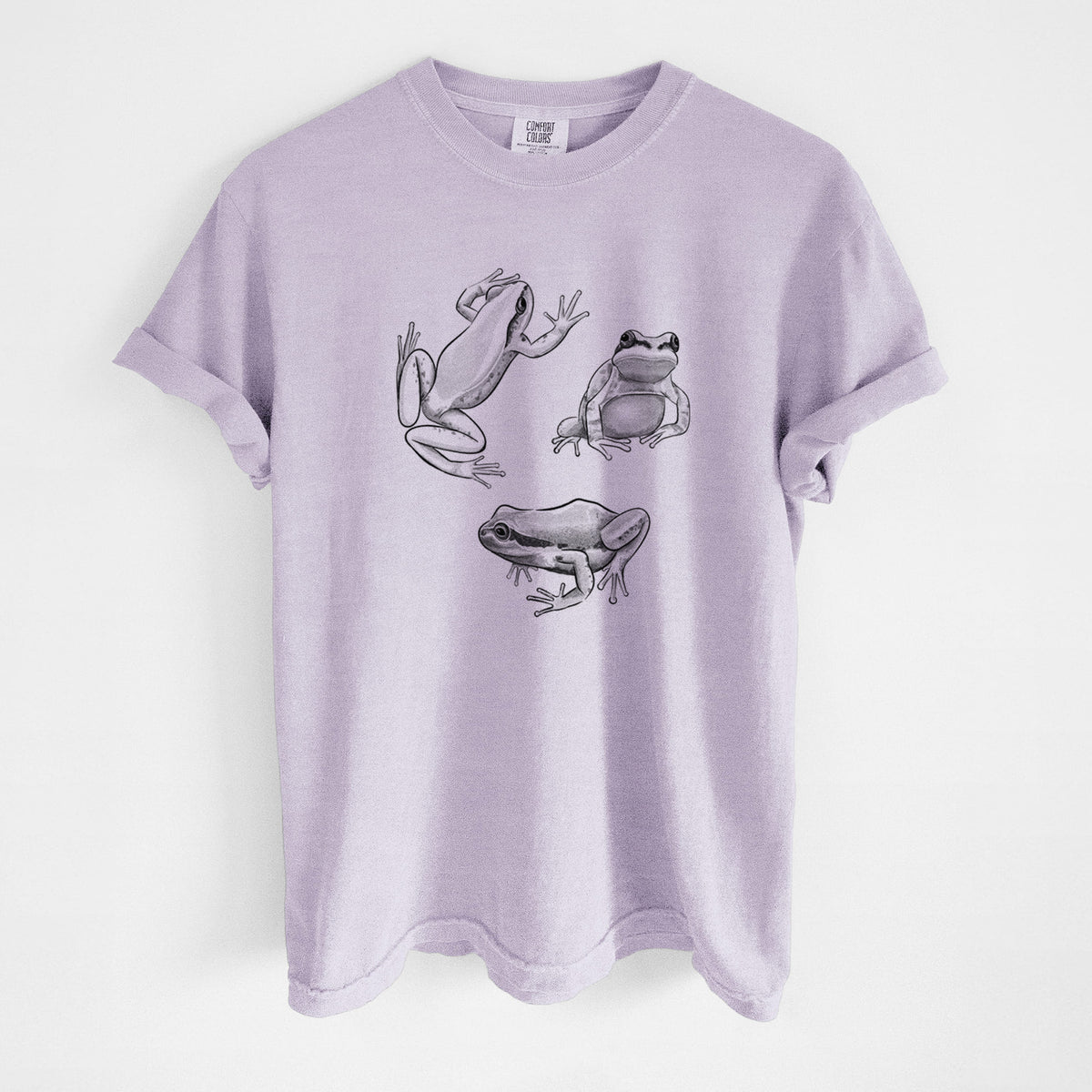 Orchid purple Comfort Colors t-shirt laid flat, printed with a black ink illustration of three Pacific tree frogs in different poses.