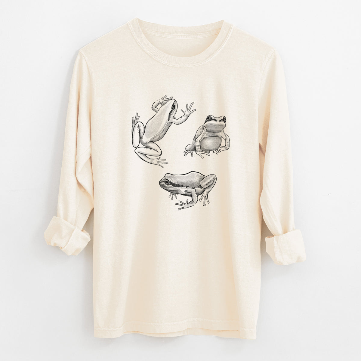 Ivory Comfort Colors long sleeve shirt laid flat with the cuffs rolled, printed with a black ink illustration of three Pacific tree frogs in different poses.