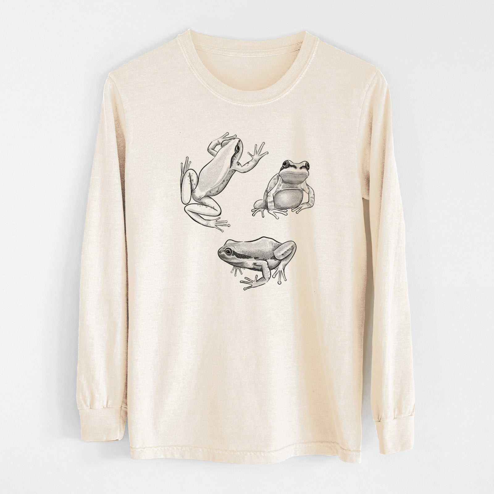 Ivory Comfort Colors long sleeve shirt laid flat, printed with a black ink illustration of three Pacific tree frogs in different poses.