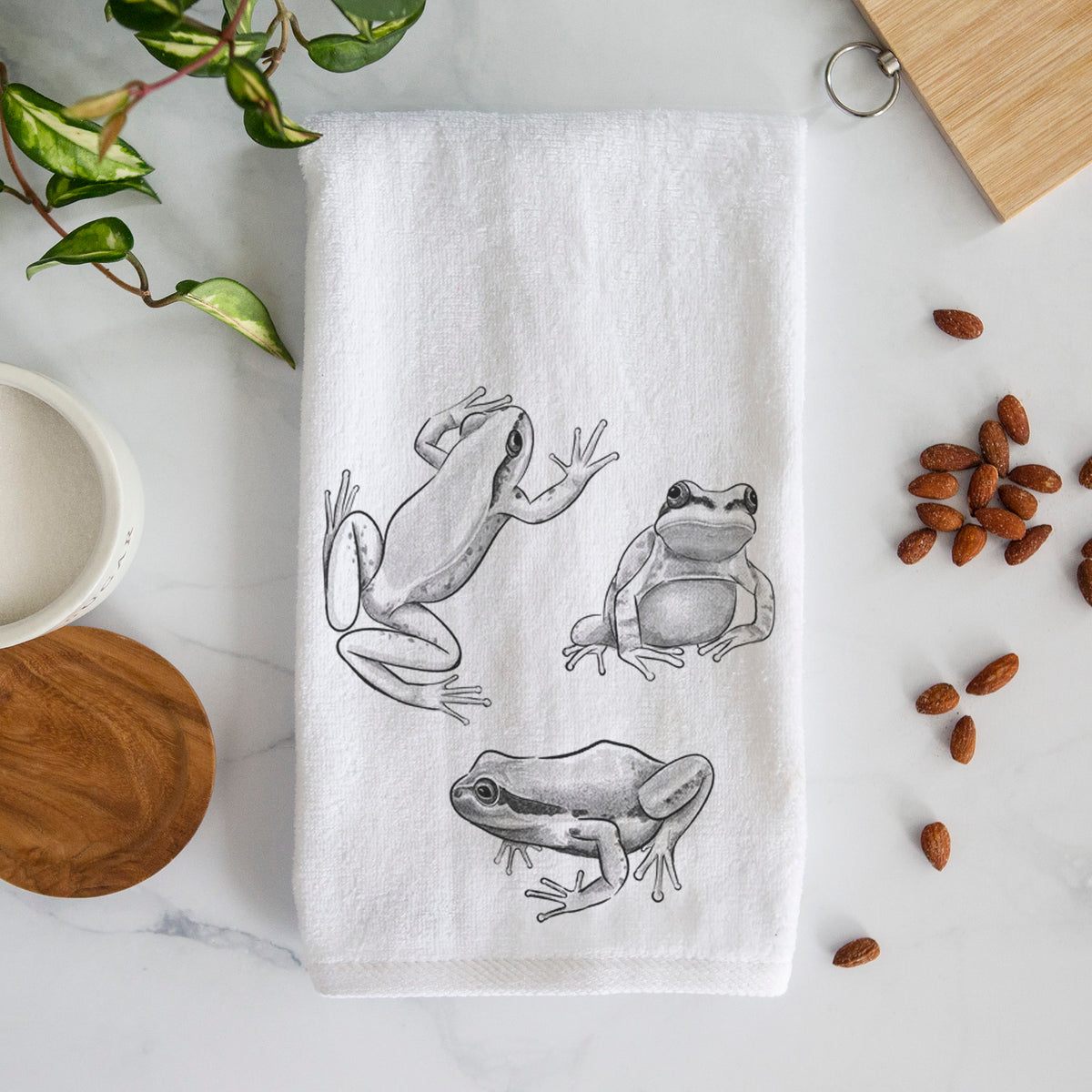 White hand towel printed with a black ink illustration of three Pacific tree frogs in different poses.