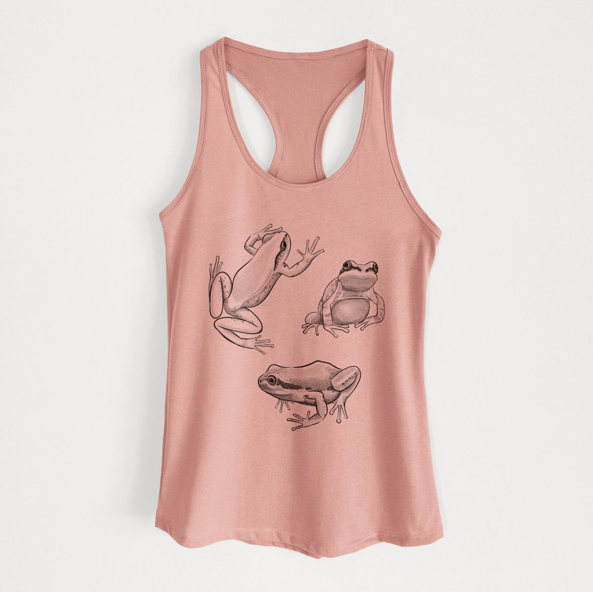 Desert pink women's racerback tank top laid flat, printed with a black ink illustration of three Pacific tree frogs in different poses.