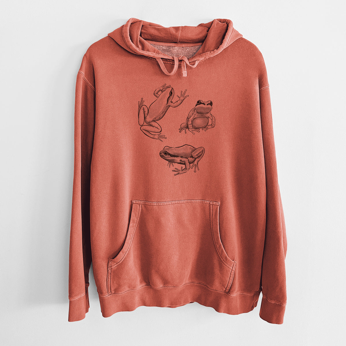 Amber orange pigment dyed hoodie laid flat, printed with a black ink illustration of three Pacific tree frogs in different poses.