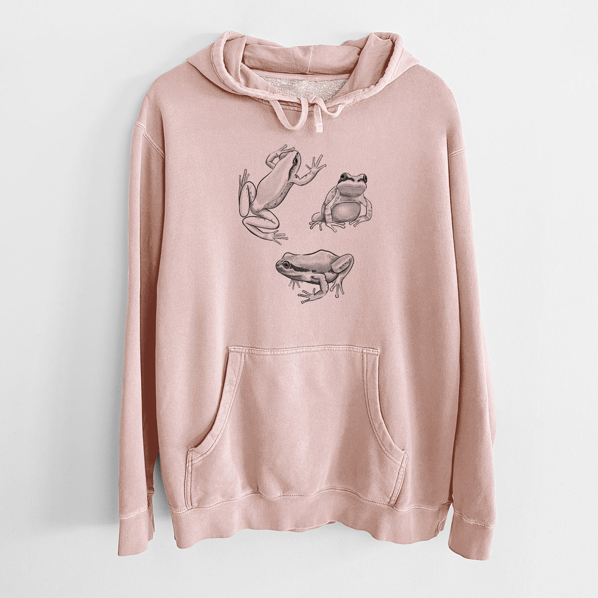 Dusty pink pigment dyed hoodie laid flat, printed with a black ink illustration of three Pacific tree frogs in different poses.