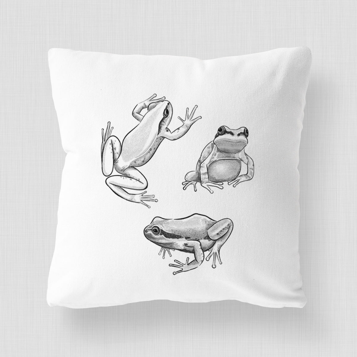 White pillow cover printed with a black ink illustration of three Pacific tree frogs in different poses.