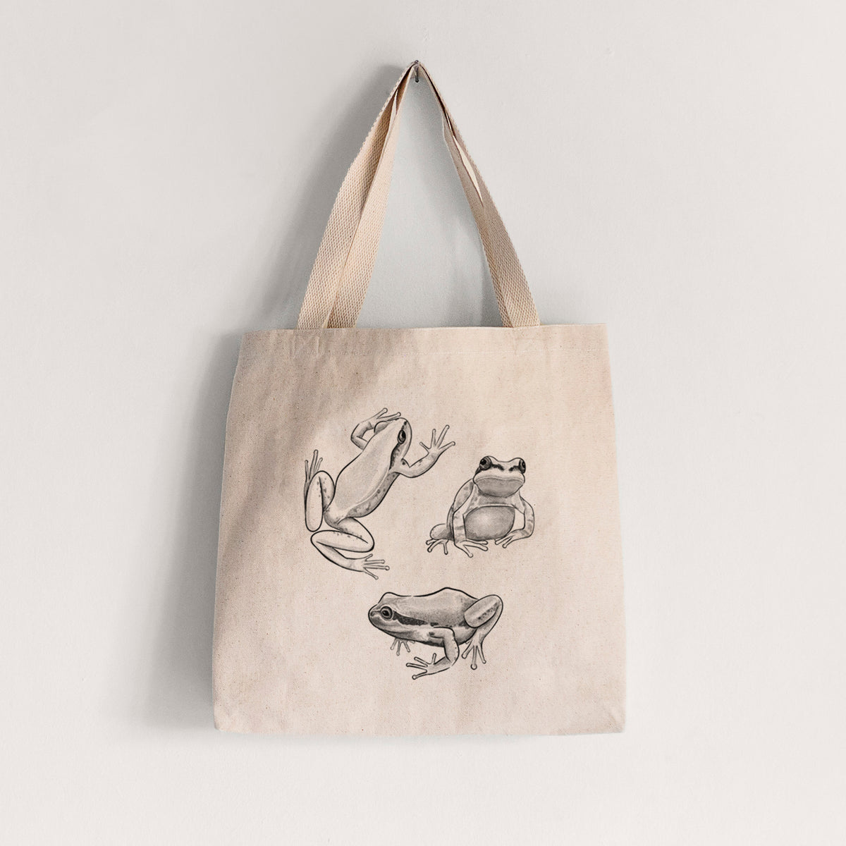 Natural canvas tote bag printed with a black ink illustration of three Pacific tree frogs in different poses.