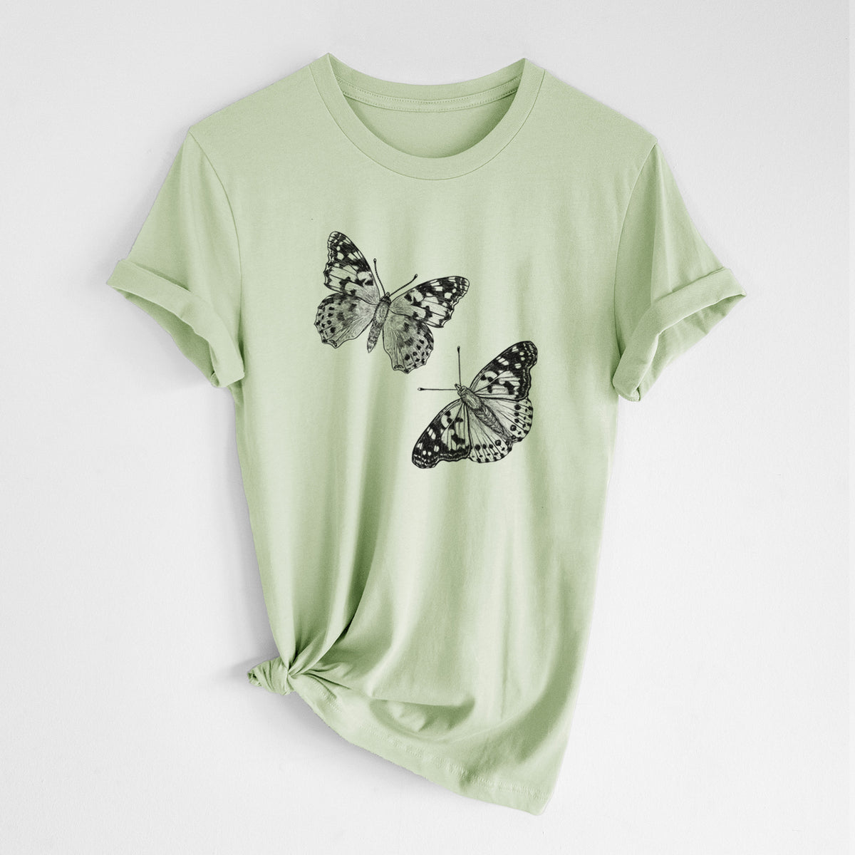 Spring green lightweight cotton t-shirt laid flat with the sleeves rolled, printed with a detailed black ink illustration of two painted lady butterflies.