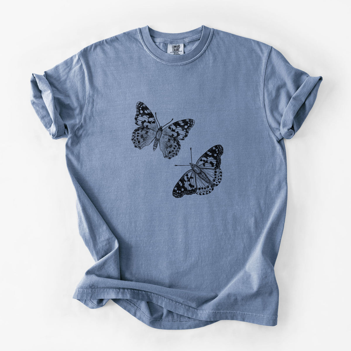 Blue jean Comfort Colors t-shirt laid flat, printed with a detailed black ink illustration of two painted lady butterflies.