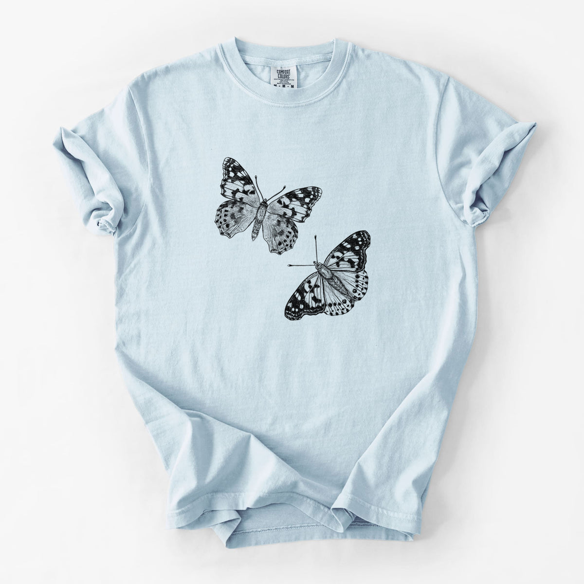 Chambray blue Comfort Colors t-shirt laid flat, printed with a detailed black ink illustration of two painted lady butterflies.