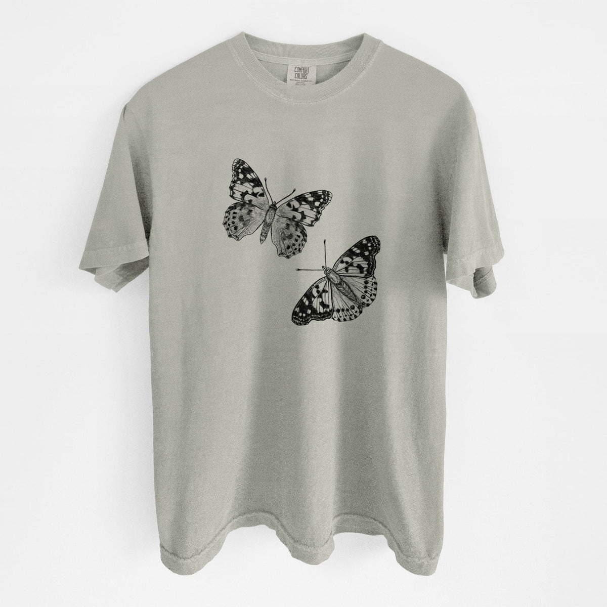 Sandstone beige Comfort Colors t-shirt laid flat, printed with a detailed black ink illustration of two painted lady butterflies.