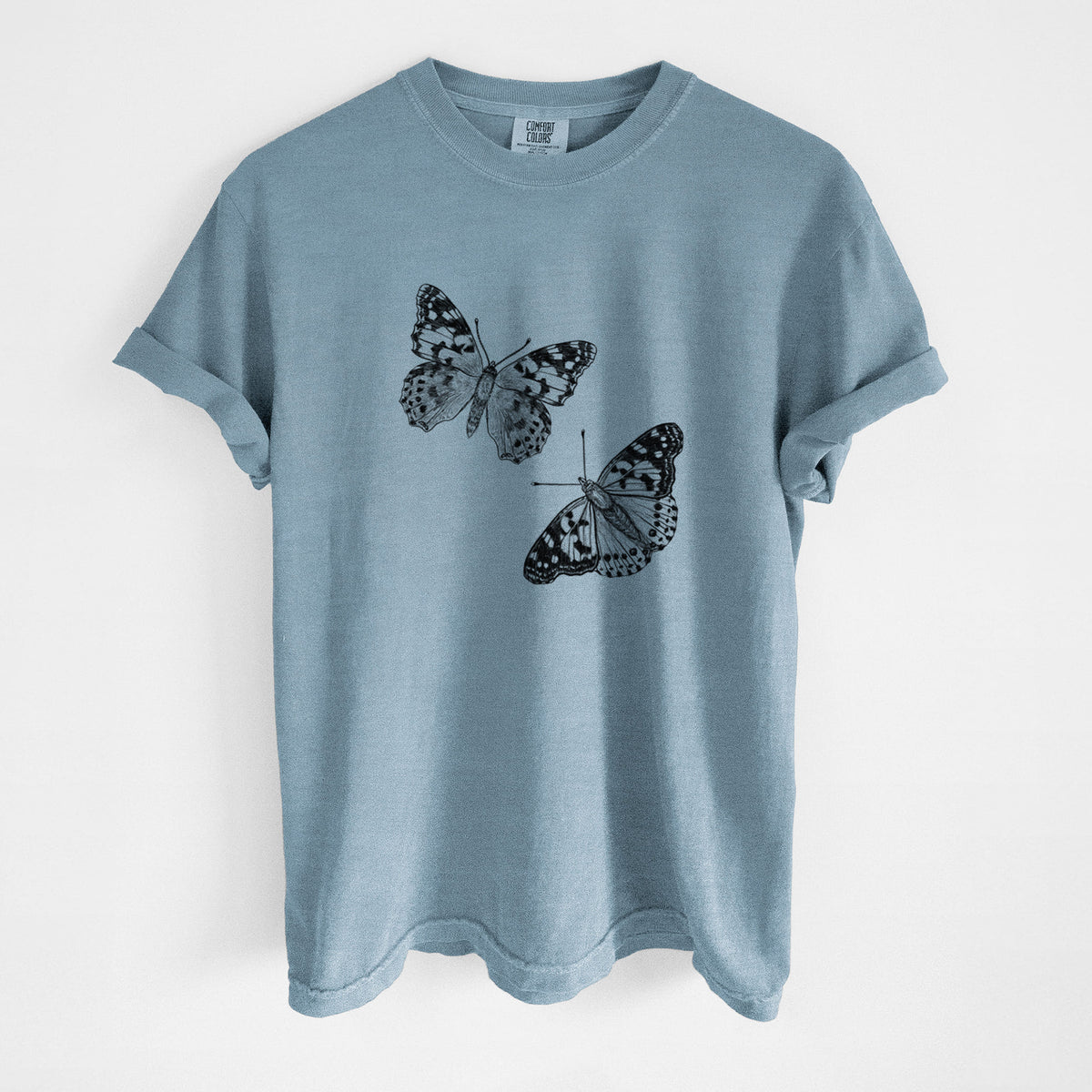 Steel blue Comfort Colors t-shirt laid flat, printed with a detailed black ink illustration of two painted lady butterflies.