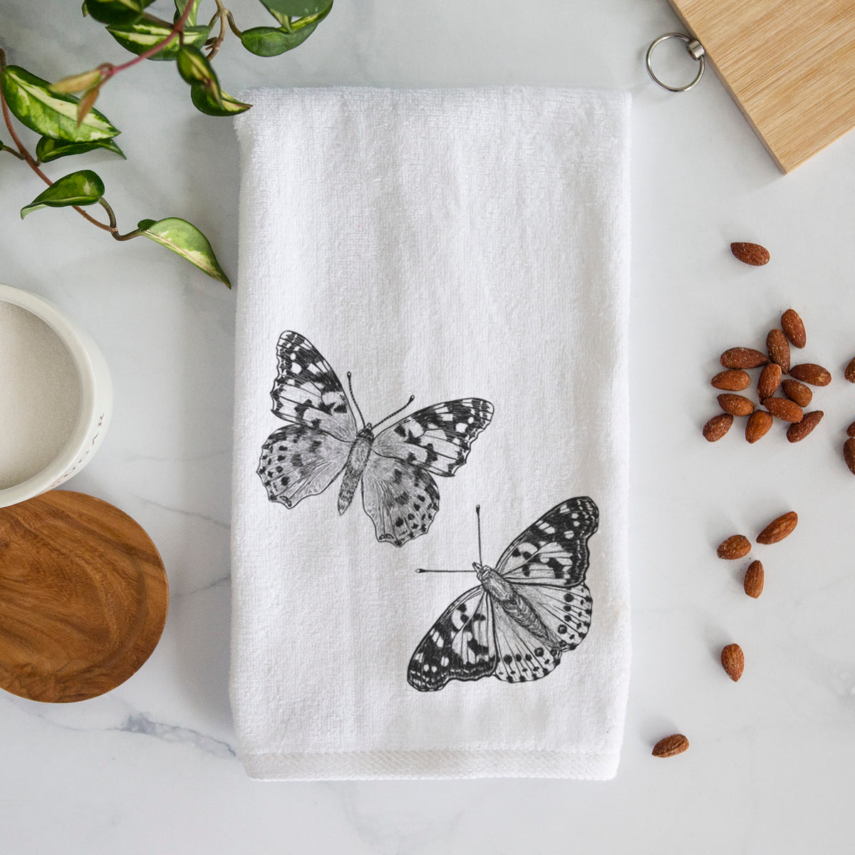 White hand towel printed with a detailed black ink illustration of two painted lady butterflies.