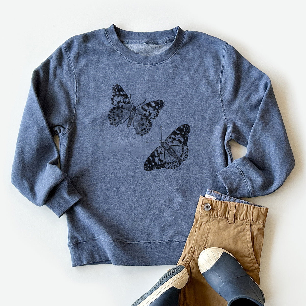 Youth crewneck sweatshirt printed with a detailed black ink illustration of two painted lady butterflies, styled flat with khaki pants and shoes.