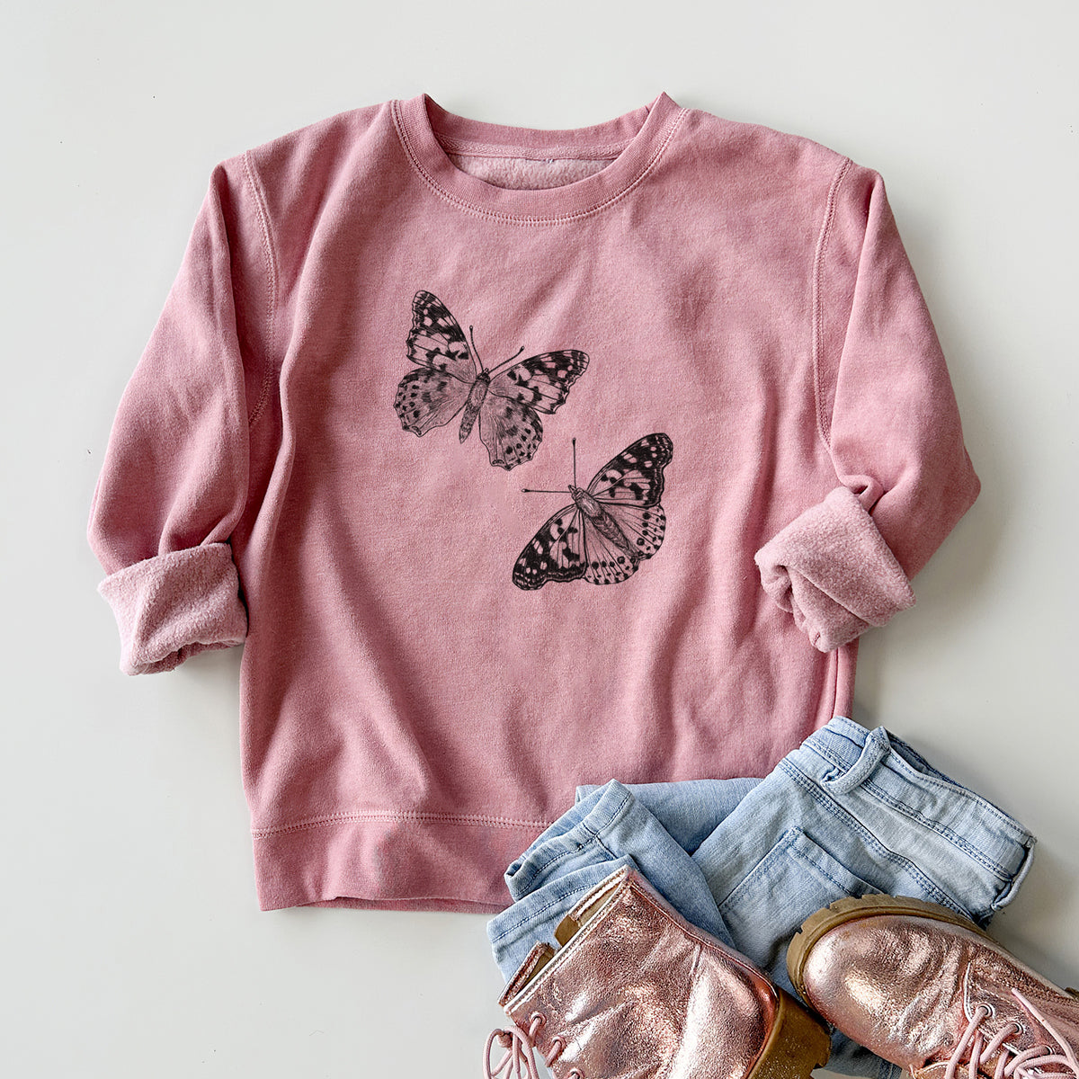Youth crewneck sweatshirt printed with a detailed black ink illustration of two painted lady butterflies, styled flat with jeans and boots.
