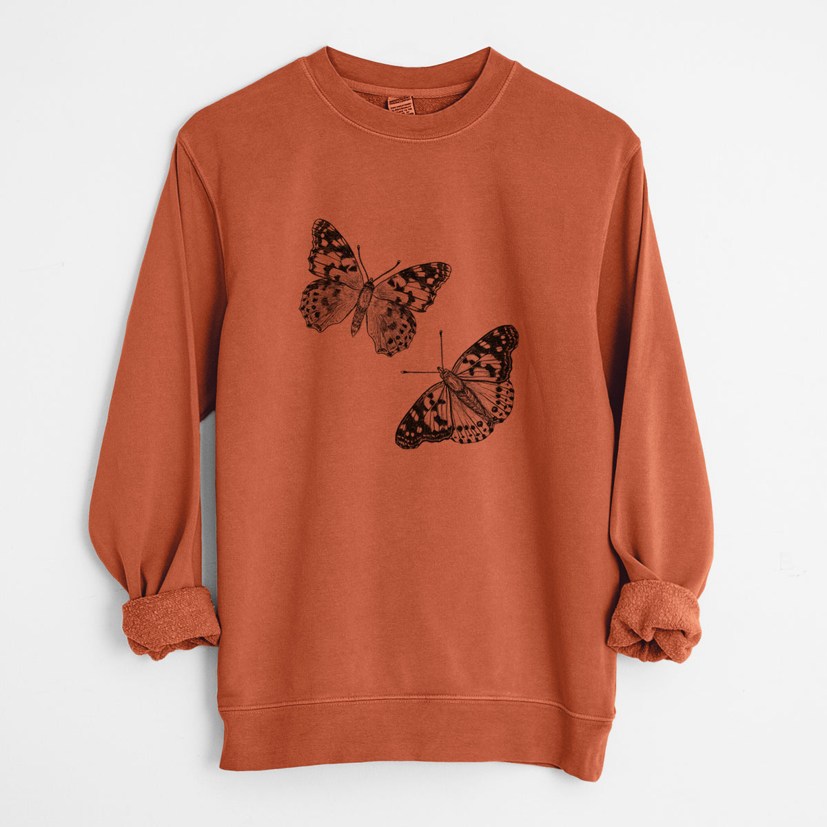 Amber orange pigment dyed crewneck sweatshirt laid flat with the sleeves rolled, printed with a detailed black ink illustration of two painted lady butterflies.