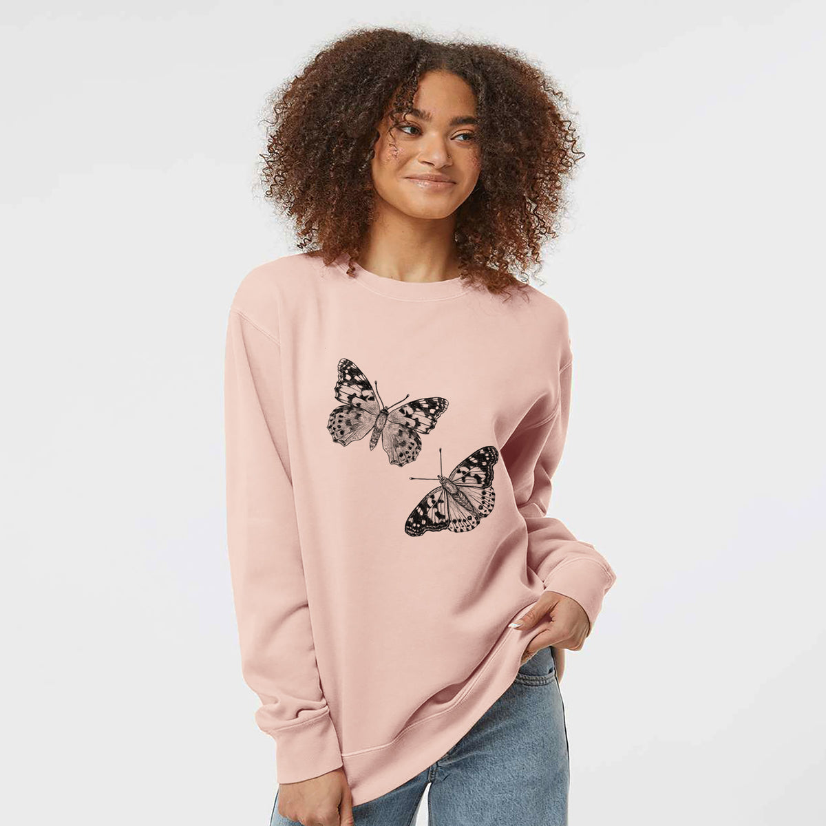 Model wearing a dusty pink pigment dyed crewneck sweatshirt printed with a detailed black ink illustration of two painted lady butterflies.