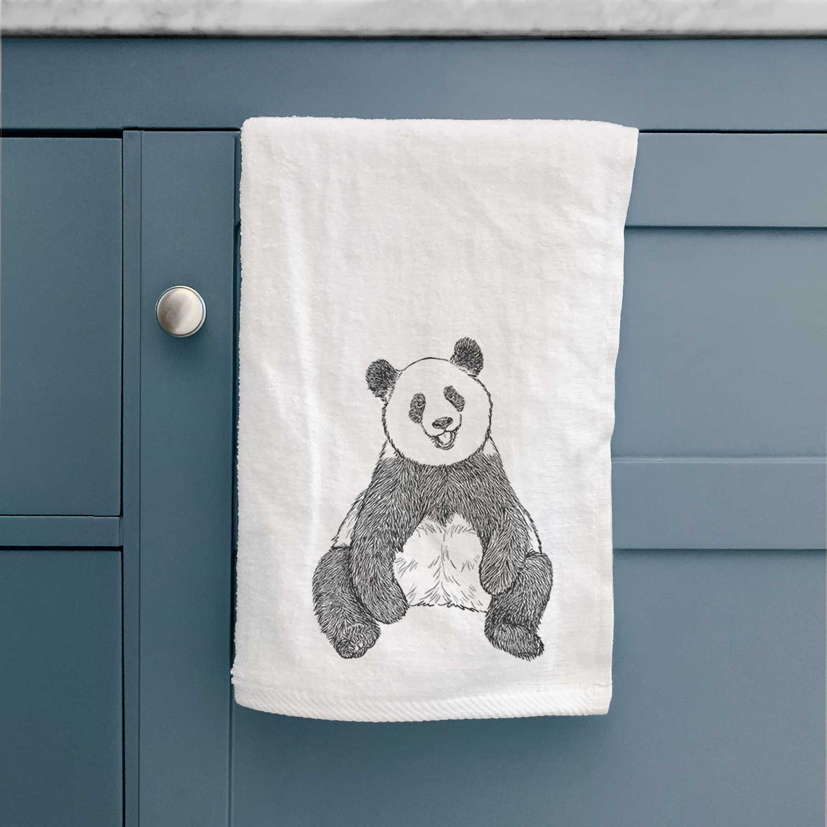 White hand towel printed with a black ink illustration of a giant panda sitting and facing forward, hanging on a cabinet door.