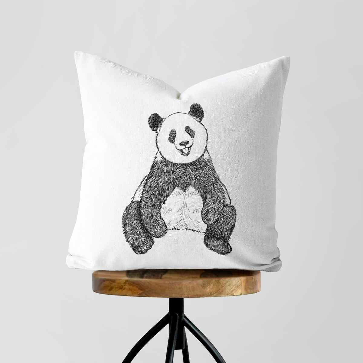 White pillow cover printed with a black ink illustration of a giant panda sitting and facing forward, on a wooden stool.