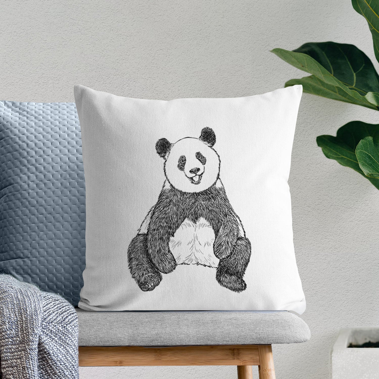 White pillow cover printed with a black ink illustration of a giant panda sitting and facing forward, on a bench beside plants.