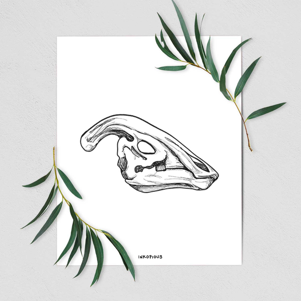 Art print of a detailed black ink illustration of a crested Parasaurolophus skull, shown with eucalyptus leaves.