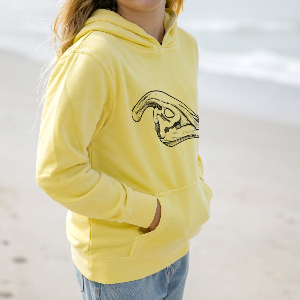 Girl wearing a youth pigment dyed hoodie printed with a detailed black ink illustration of a crested Parasaurolophus skull.