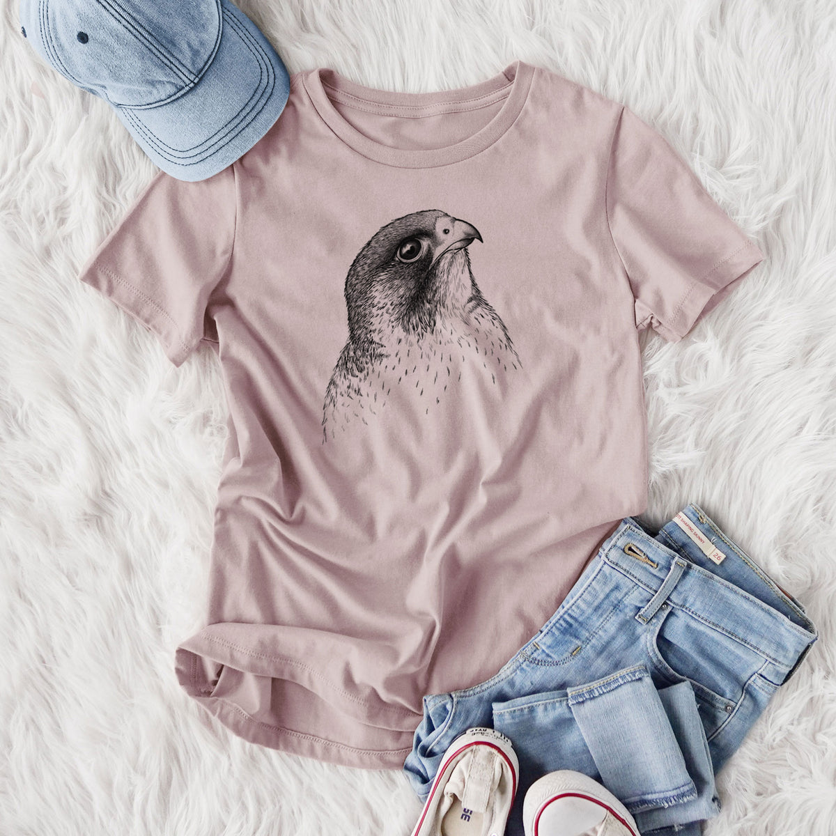 Women's relaxed fit cotton t-shirt printed with a detailed black ink portrait of a peregrine falcon's head, styled flat on a white faux fur rug with jeans.