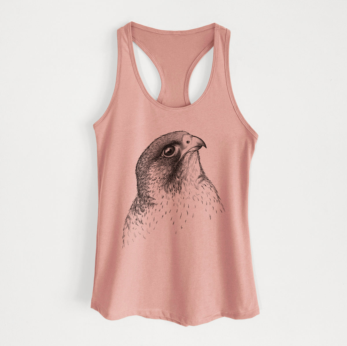 Desert pink women's racerback tank top laid flat, printed with a detailed black ink portrait of a peregrine falcon's head.