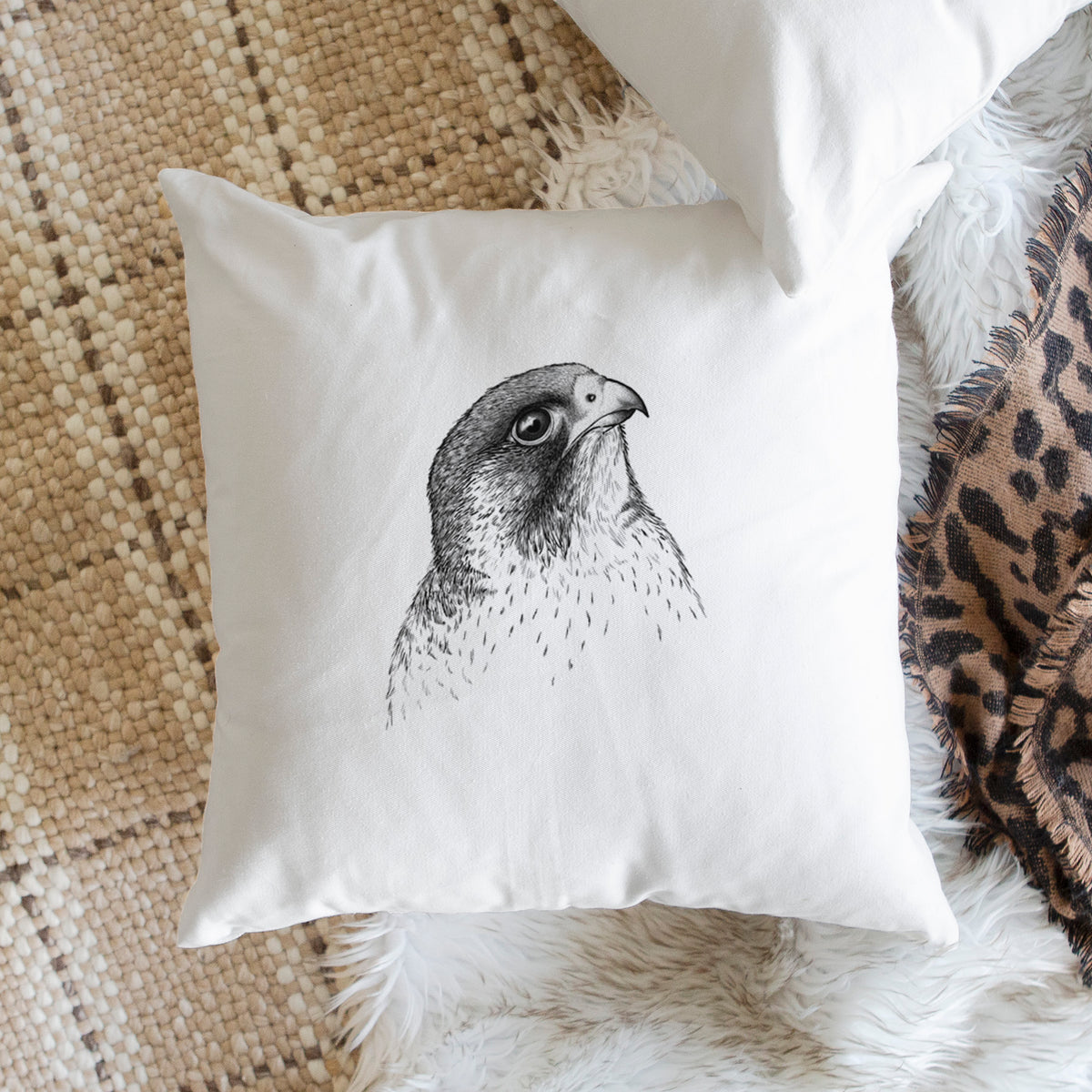White pillow cover printed with a detailed black ink portrait of a peregrine falcon's head, on a woven chair.