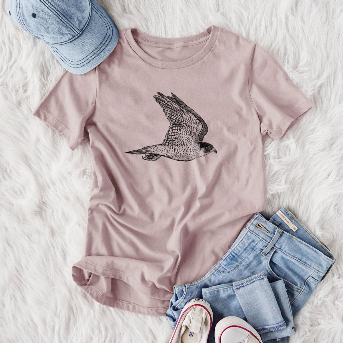 Women's relaxed fit cotton t-shirt printed with a detailed black ink illustration of a peregrine falcon in flight, styled flat on a white faux fur rug with jeans.