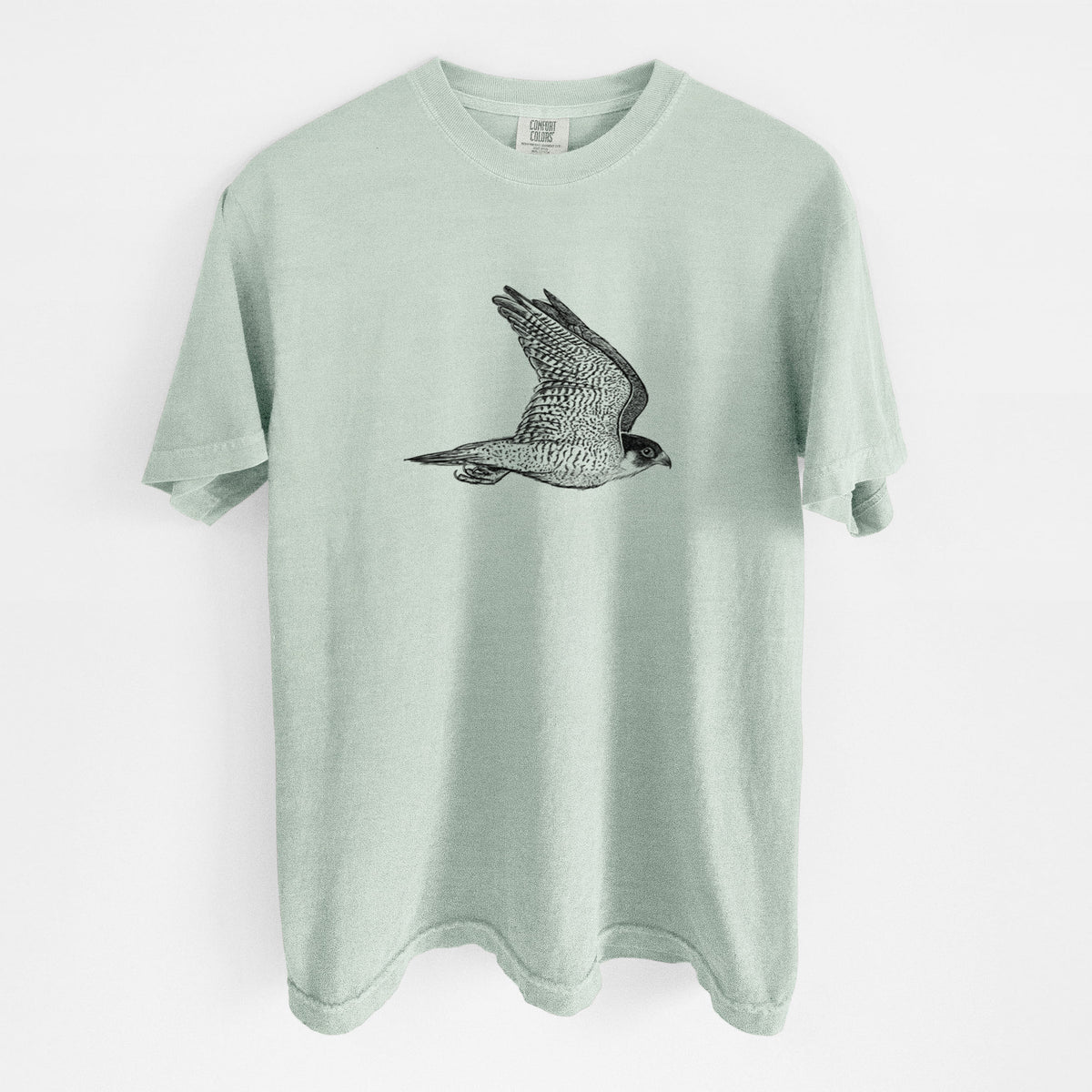 Bay green Comfort Colors t-shirt laid flat, printed with a detailed black ink illustration of a peregrine falcon in flight.