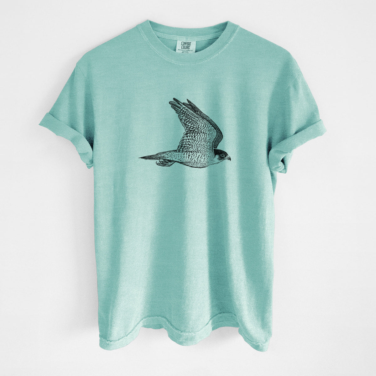 Chalky mint Comfort Colors t-shirt laid flat, printed with a detailed black ink illustration of a peregrine falcon in flight.