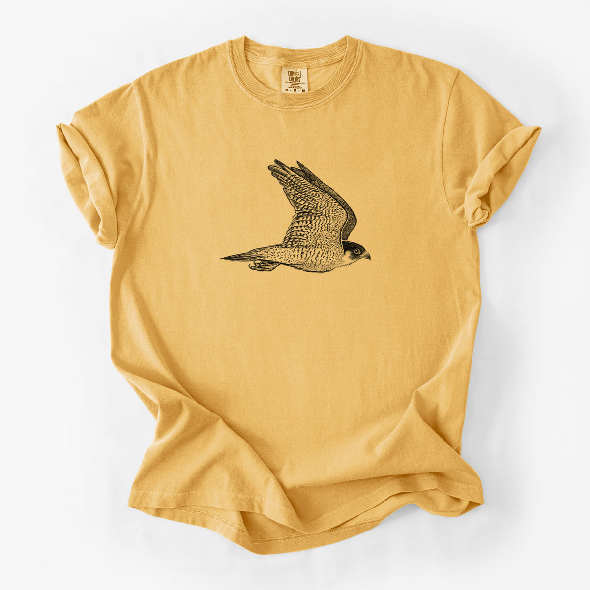 Golden wheat yellow Comfort Colors t-shirt laid flat, printed with a detailed black ink illustration of a peregrine falcon in flight.