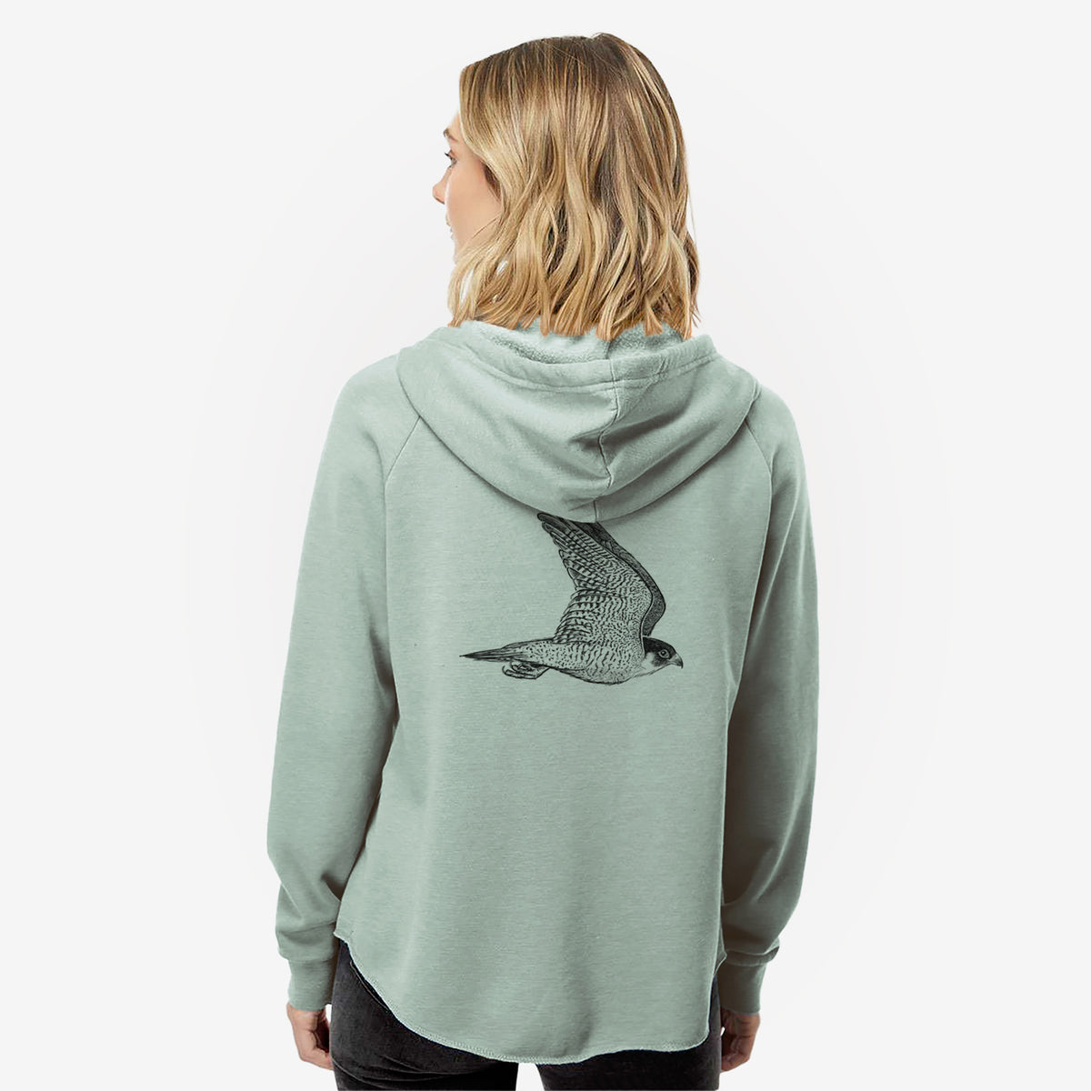 Woman wearing a sage green women's Cali Wave zip-up sweatshirt printed with a detailed black ink illustration of a peregrine falcon in flight, seen from behind.