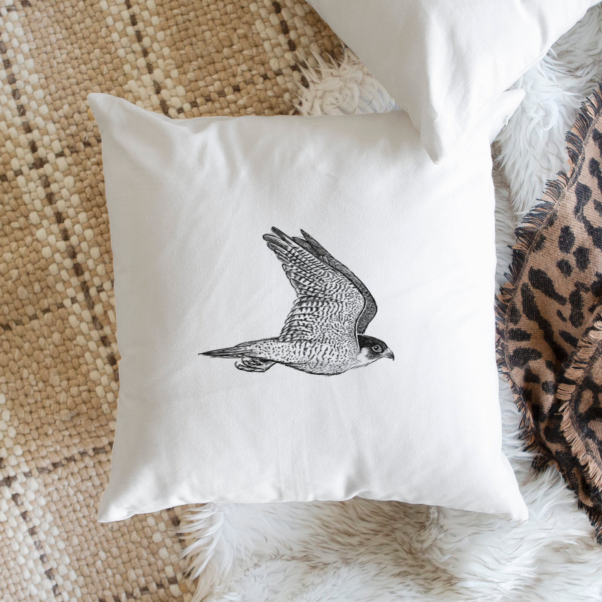 White pillow cover printed with a detailed black ink illustration of a peregrine falcon in flight, on a woven chair.