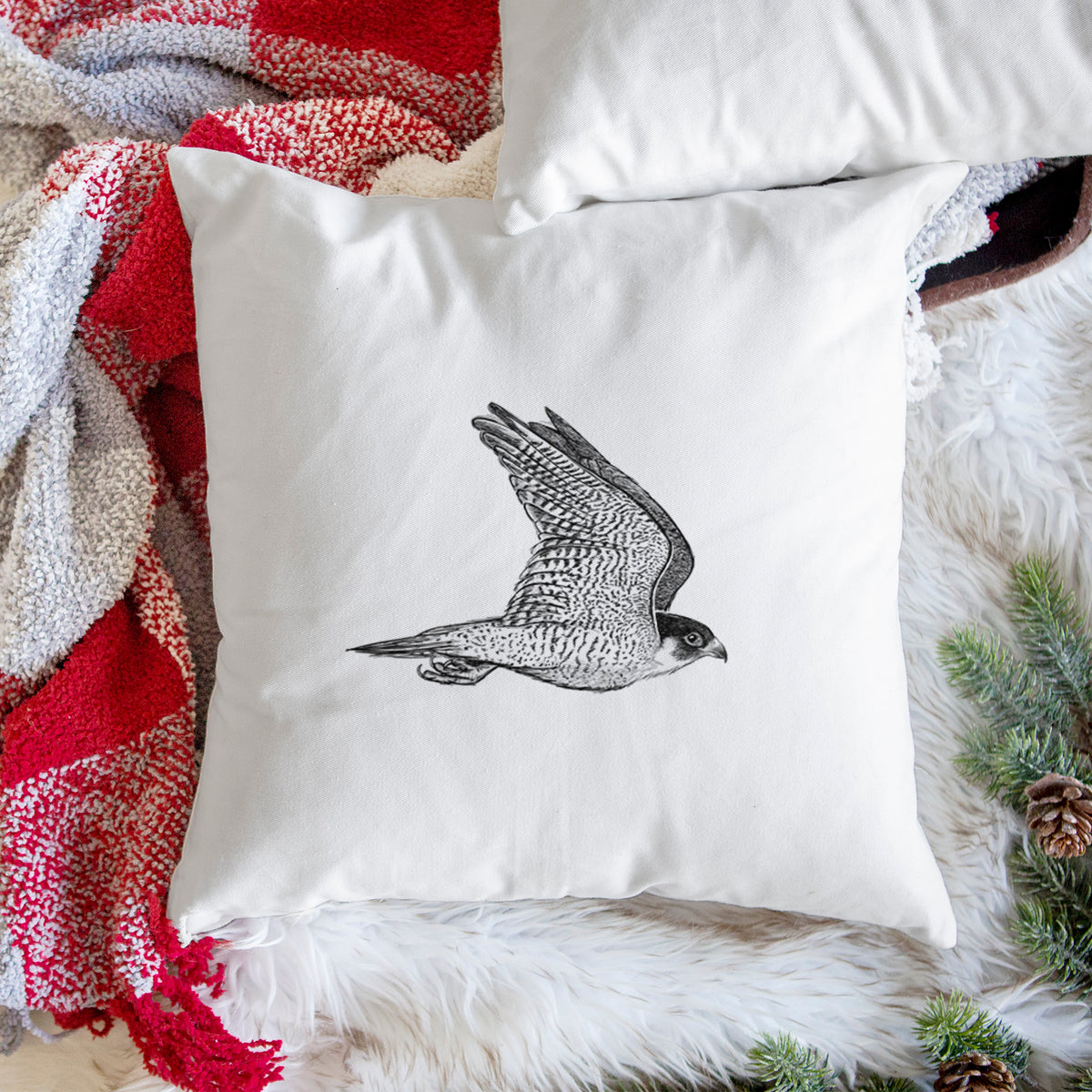 White pillow cover printed with a detailed black ink illustration of a peregrine falcon in flight, on a woven chair.