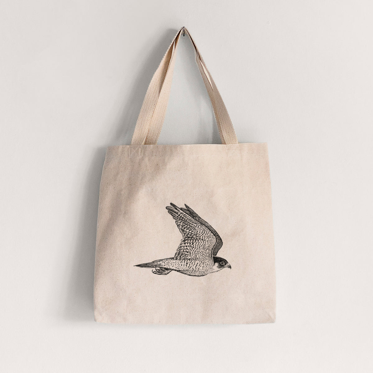 Natural canvas tote bag printed with a detailed black ink illustration of a peregrine falcon in flight.