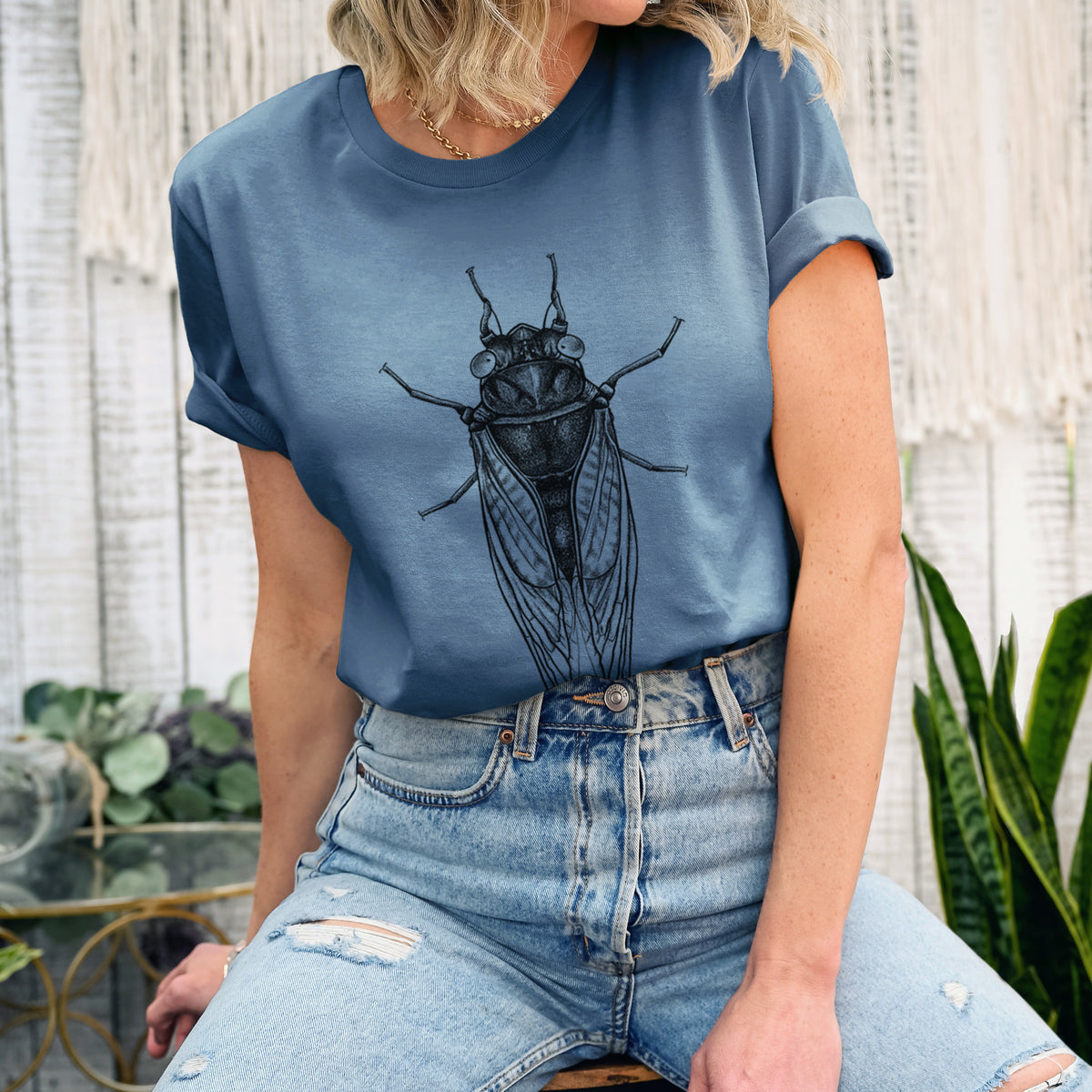 Woman wearing a steel blue lightweight cotton t-shirt printed with a detailed black ink illustration of a periodical cicada with its wings folded, seen from above.