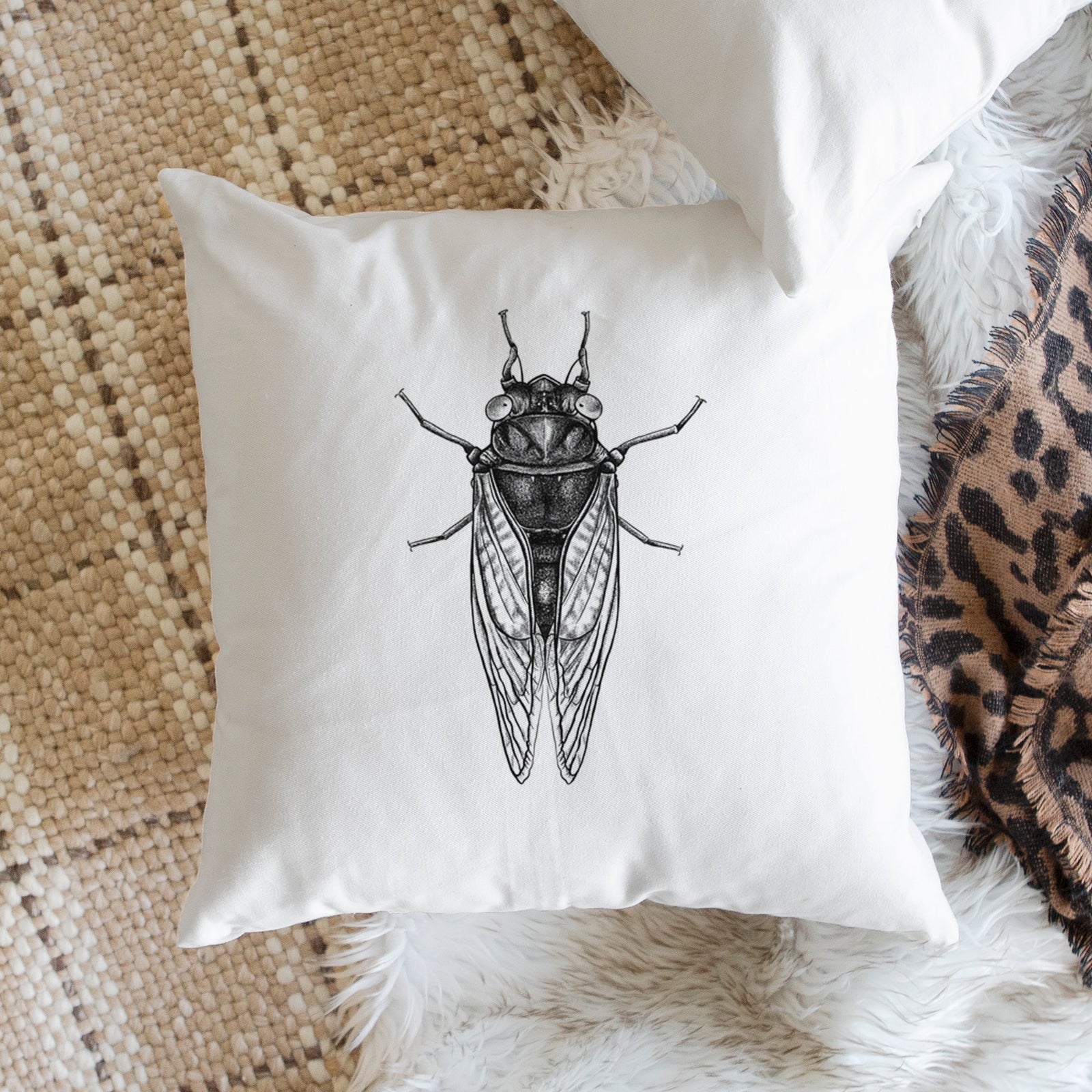 White pillow cover printed with a detailed black ink illustration of a periodical cicada with its wings folded, seen from above, on a bench beside plants.