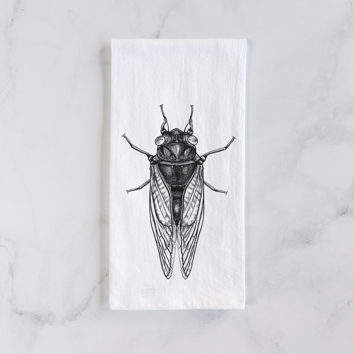 White cotton tea towel laid flat on marble, printed with a detailed black ink illustration of a periodical cicada with its wings folded, seen from above.