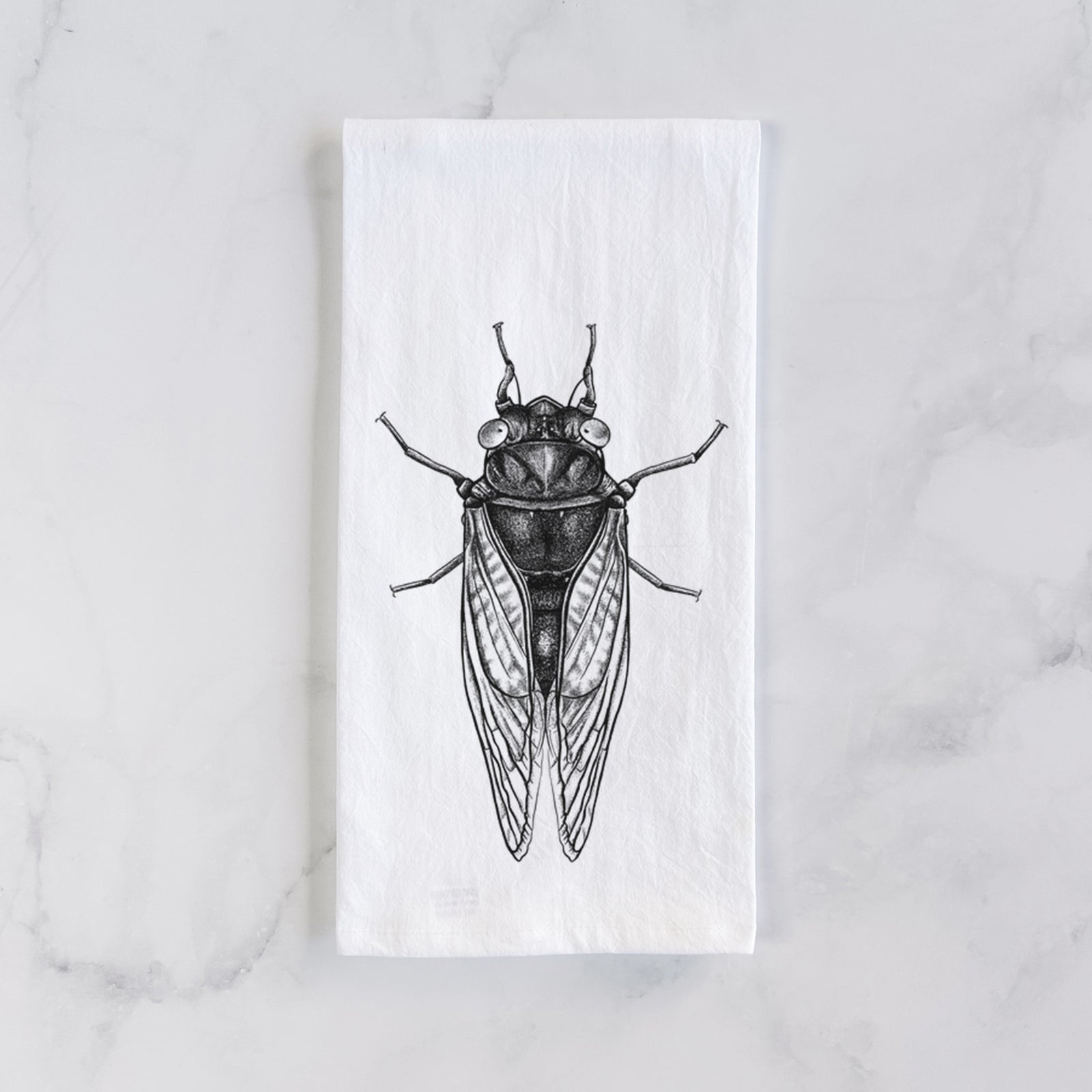 White cotton tea towel printed with a detailed black ink illustration of a periodical cicada with its wings folded, seen from above, on a marble counter beside a round wooden cutting board and greenery.