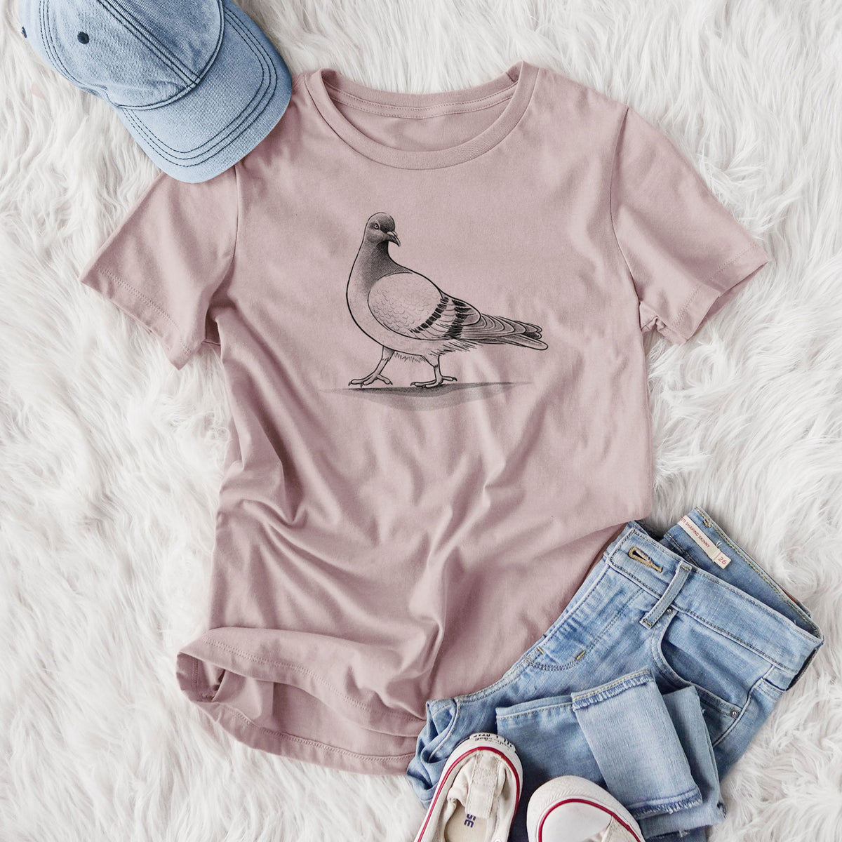 Women's relaxed fit cotton t-shirt printed with a black ink illustration of a pigeon standing, styled flat on a white faux fur rug with jeans.