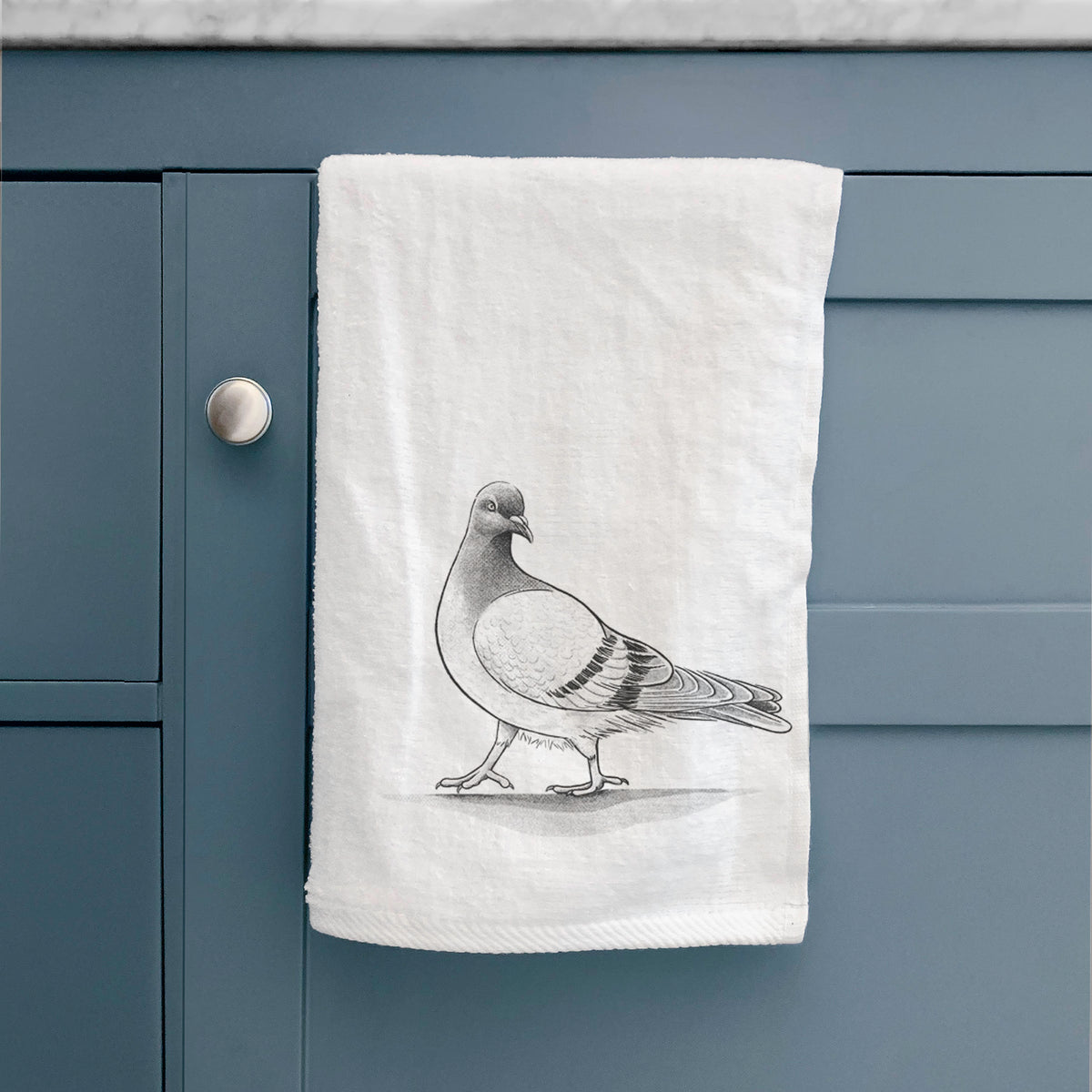 White hand towel printed with a black ink illustration of a pigeon standing, hanging on a cabinet door.