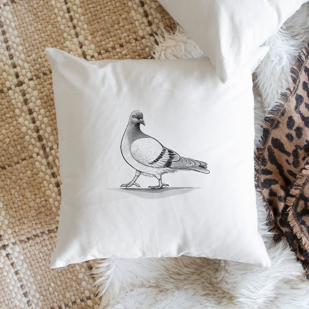 White pillow cover printed with a black ink illustration of a pigeon standing, on a woven chair.