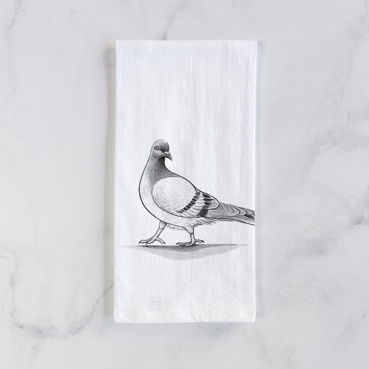 White cotton tea towel laid flat on marble, printed with a black ink illustration of a pigeon standing.