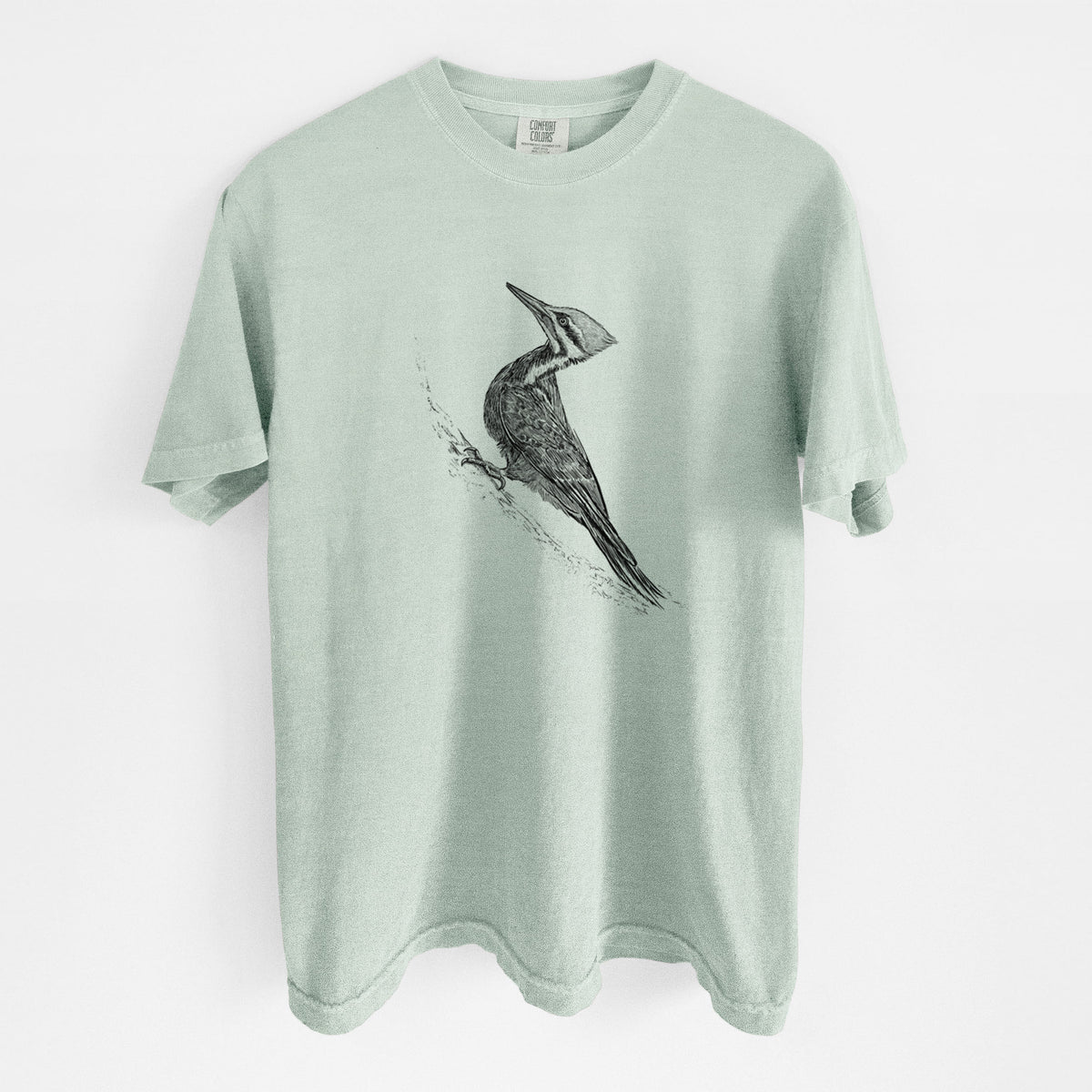 Bay green Comfort Colors t-shirt laid flat, printed with a black ink illustration of a pileated woodpecker clinging to a tree trunk.