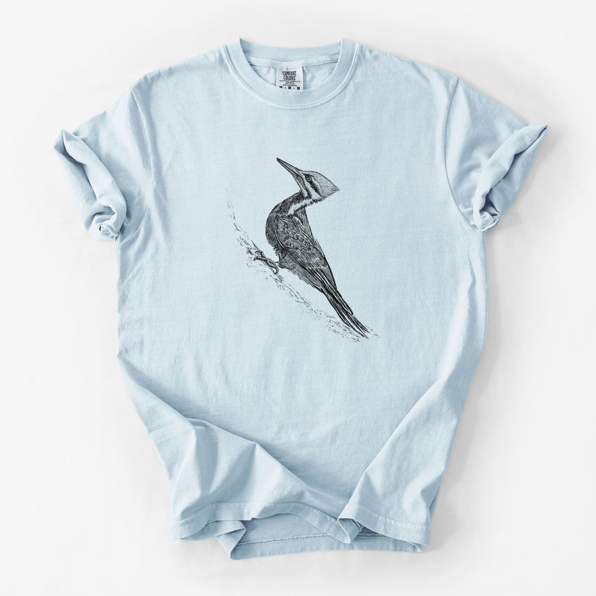 Chambray blue Comfort Colors t-shirt laid flat, printed with a black ink illustration of a pileated woodpecker clinging to a tree trunk.