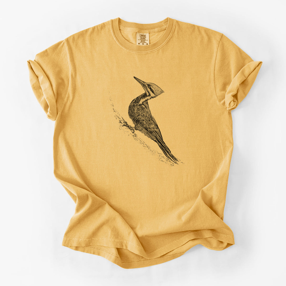 Golden wheat yellow Comfort Colors t-shirt laid flat, printed with a black ink illustration of a pileated woodpecker clinging to a tree trunk.