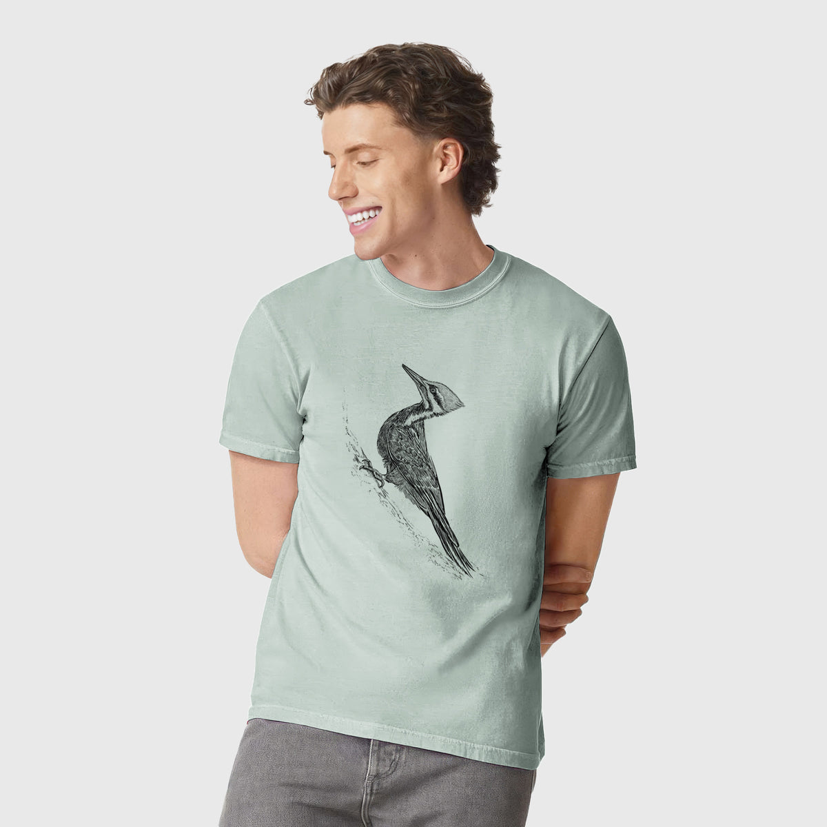 Man wearing a Comfort Colors t-shirt printed with a black ink illustration of a pileated woodpecker clinging to a tree trunk.