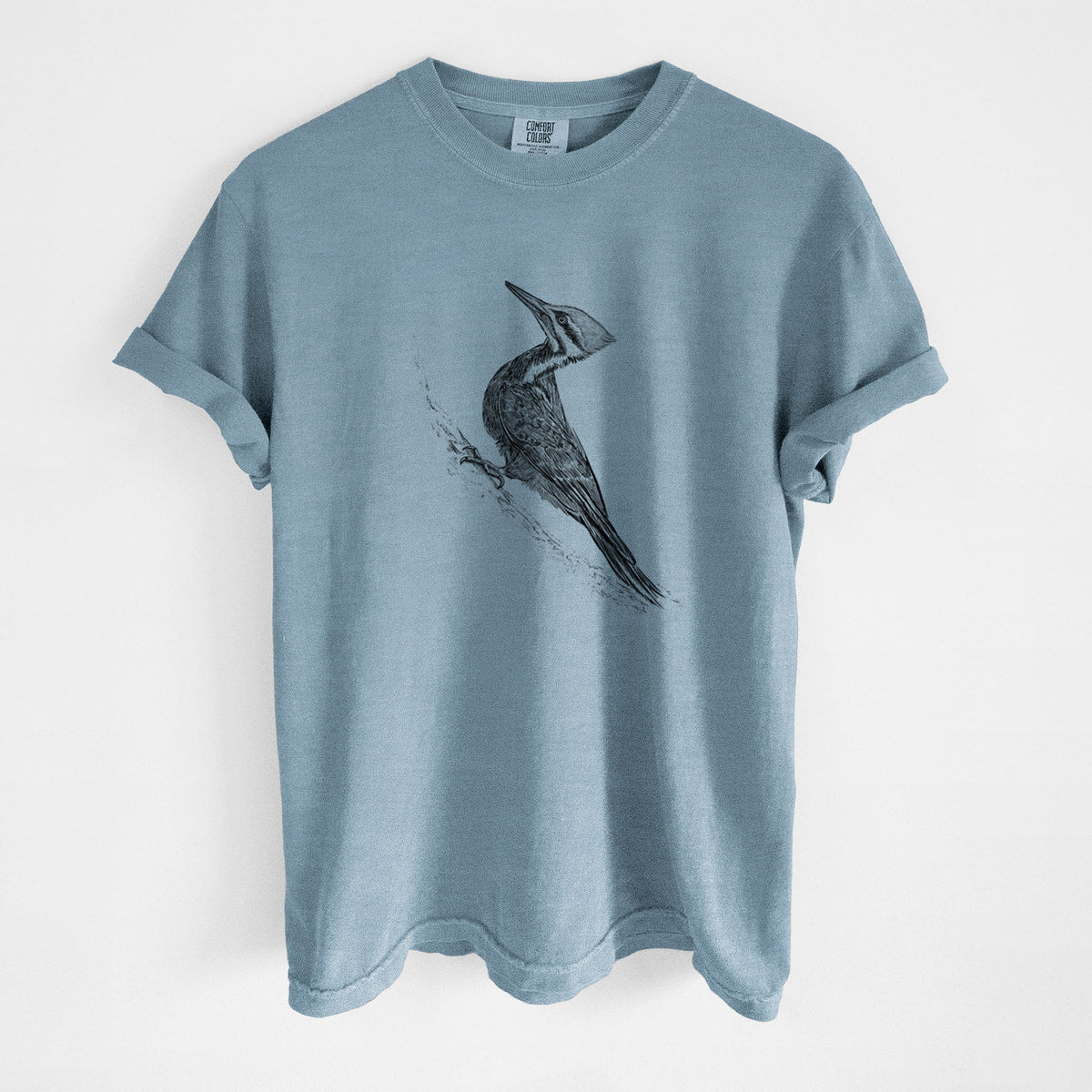 Steel blue Comfort Colors t-shirt laid flat, printed with a black ink illustration of a pileated woodpecker clinging to a tree trunk.
