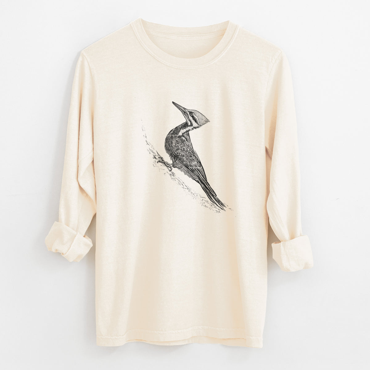 Ivory Comfort Colors long sleeve shirt laid flat with the cuffs rolled, printed with a black ink illustration of a pileated woodpecker clinging to a tree trunk.